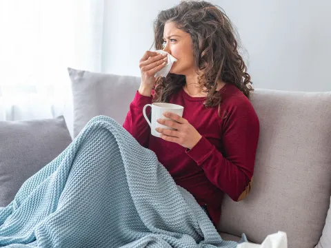 A woman on her couch blowing her nose. 