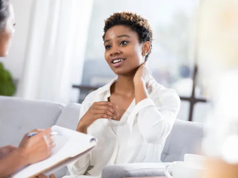 A young woman rubs her neck as she talks to a nurse