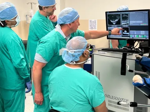 People in scrubs in operating room, pointing to screen.