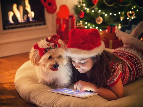 Young girl playing on tablet with dog next to her during the holidays