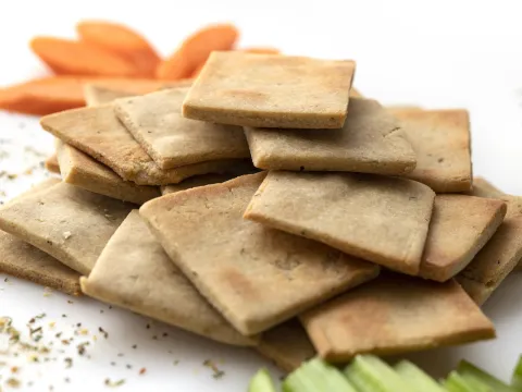 Pile of square crackers next to celery and carrot sticks