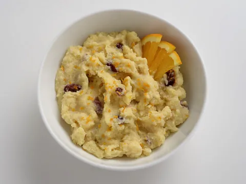 a bowl of polenta with dried cranberries and orange slices