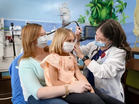 Dr. Kirby checking the ear of a pediatric patient while she sits on her mother's lap.