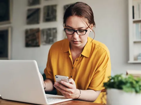 A woman on her laptop while using her phone