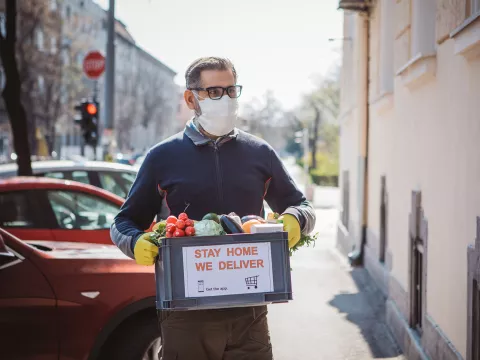 A man in a mask and gloves delivering groceries.