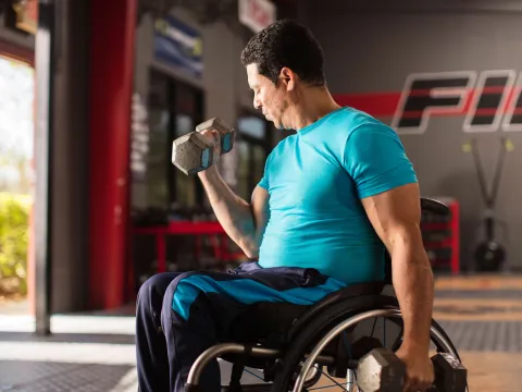 Man in a wheelchair lifting a dumbbell weight with his right hand.