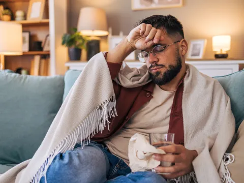 Man sitting at home on the couch wrapped in a blanket while sick with the flu.