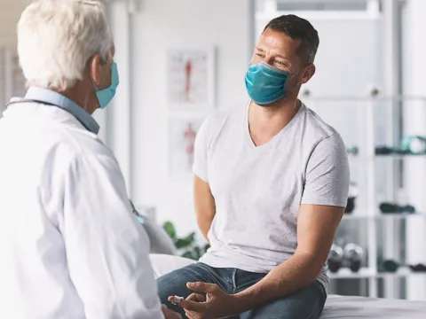 Man talking with talking while both are wearing masks.