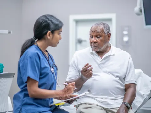 Man talking with a nurse, during an appointment, inside of an examination room.