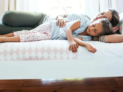 A mother and daughter laying down on a bed in their house