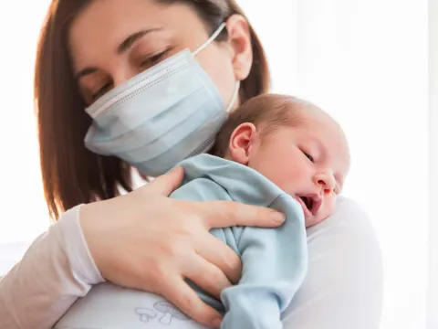 A mom wearing a mask holding her infant.