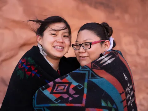 Native American mother and daughter wrapped in a blanket together while outdoors.