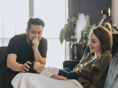 Mother with her baby on her lap and father placing his hand on his baby's head while at home together.