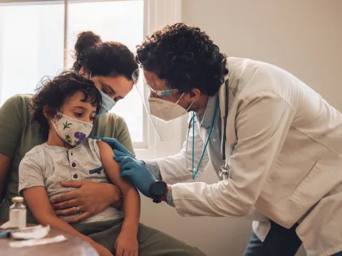 A mother holds her son while a doctor prepares to administer a vaccine.