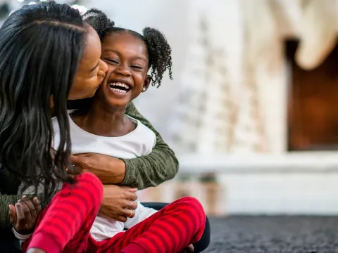 A mother hugging her daughter in front of the fireplace.