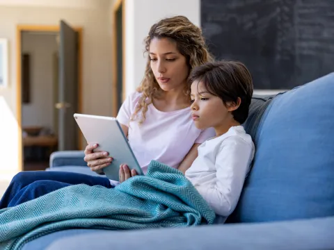 A mother and son sitting on a couch and using a tablet.