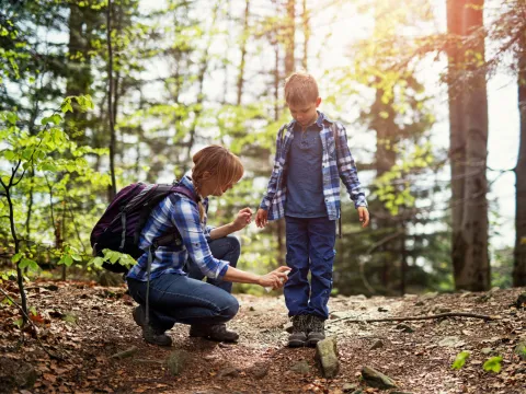 A mother spraying her son with bug spray while on a hike in the woods.