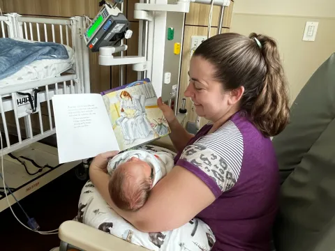 A mom reads to her baby in the AdventHealth for Children NICU in Orlando. Sitting in a rocking chair, she holds her baby while reading the book "Love You Forever."