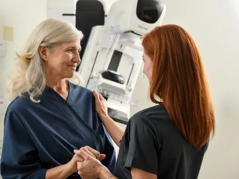 Woman with a technician before a mammogram standing in front of a mammography machine.