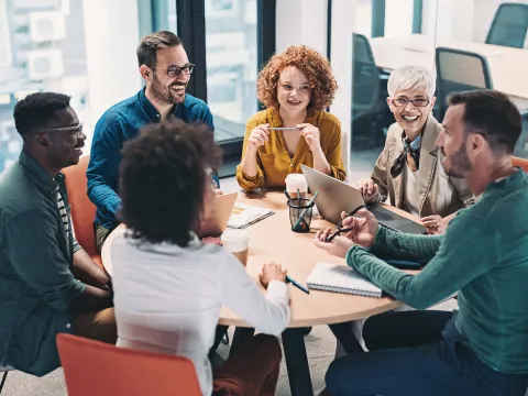 A Group of Co-Workers Sit at a Round Table and Have a Discussion About Work