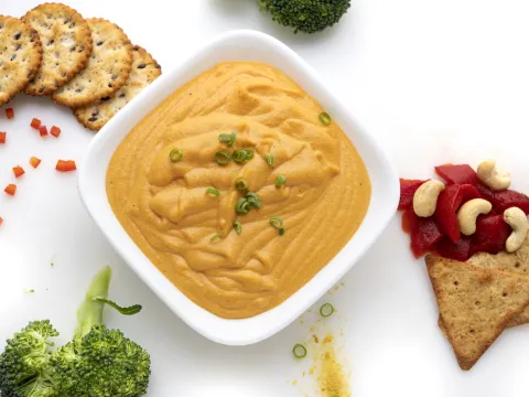 White bowl of orange cheese sauce next to crackers and broccoli.