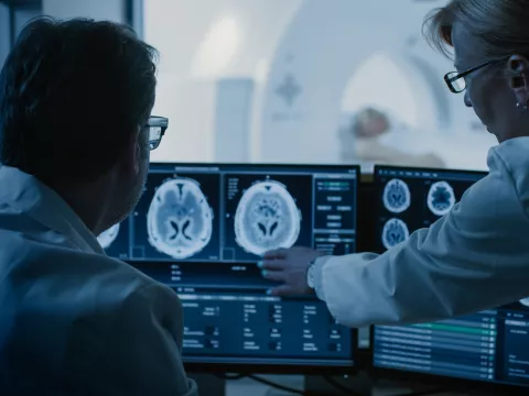 Radiologists looking at a brain scan while a patient is getting a CT scan.