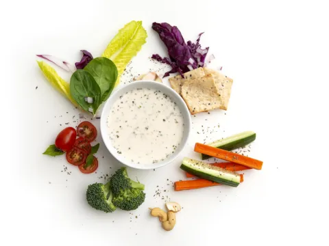 Cup of creamy ranch-style dressing surrounded by vegetables