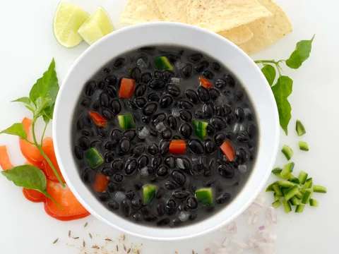 Bowl of cuban frijole stew surrounded by garnish, limes, and peppers