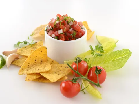 Dish of rustic tomato salsa surrounded by chips, garlic and tomatoes