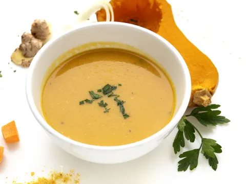 Bowl of squash soup with half butternut squash and green sprig garnish on side