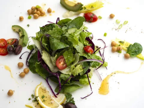 Mound of mixed green salad with tomato and lemon garnishes