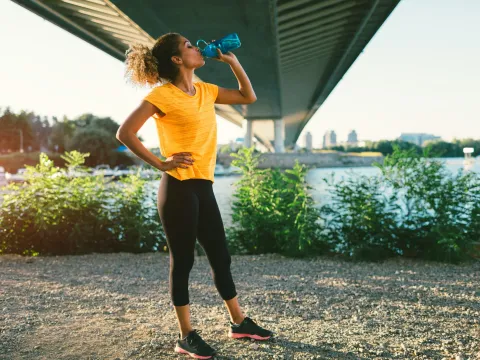 A woman drinking water on a trail, post run, during sunset.