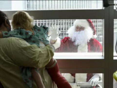 Santa Claus appears outside the sixth-floor window of AdventHealth for Children to greet a young patient.