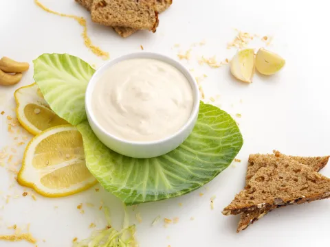 a small bowl filled with homemade mayonaise, surrounded by lettuce, lemons and crackers.