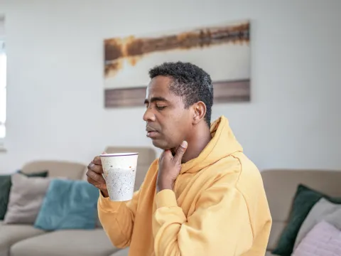 A man with a sore throat sips a cup of hot tea.