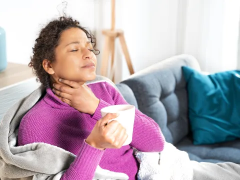 woman rubs sore throat and drinks tea