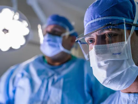 Close up of a surgeon in the foreground with another surgeon in the background in the operating room during a surgery.