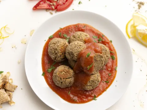 White bowl of tofu meatballs and sweet and sour sauce with lemon garnish