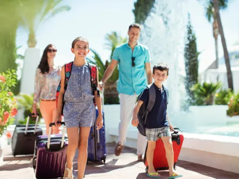 A family walks together outdoors with their luggage. 