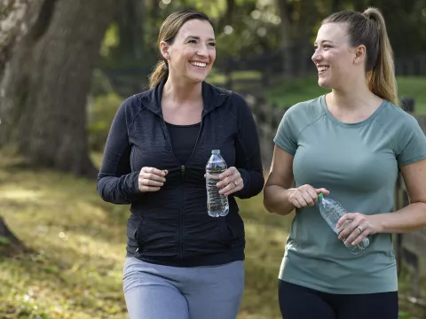 Two women holding water bottles walking together outside 