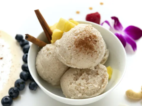 A bowl of vanilla-coconut ice cream surrounded by fresh fruit and flowers.