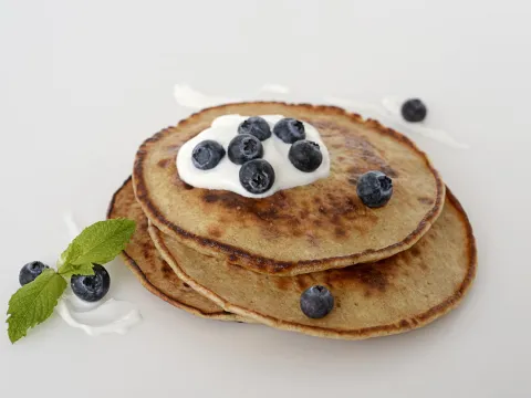 a stack of three homemade pancakes, topped with a dollop of Greek yogurt and fresh blueberries