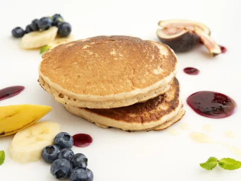 a short stack of pancakes, surrounded by fresh blueberries, banana slices and other fruit