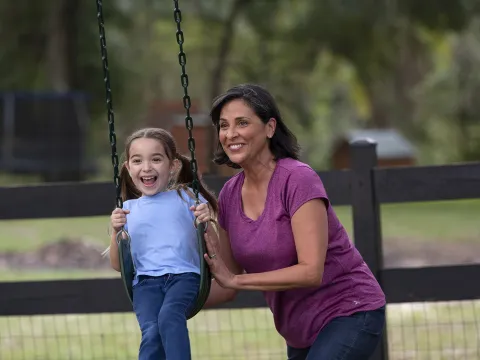 Middle aged woman pushing a little girl on a swing at the park