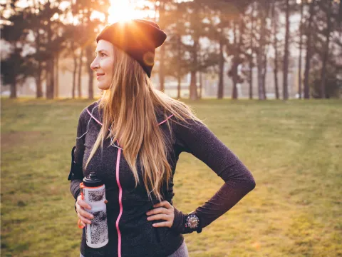 Woman wearing active wear and holding a water bottle in a park during winter.