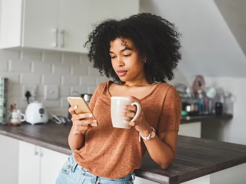 Woman during her morning routine: a cup of coffee while checking her phone.