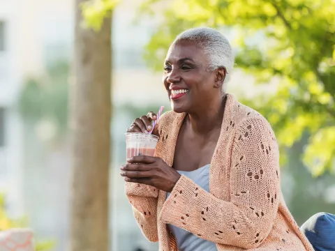 A Black Woman Enjoys a Smoothie on a Bench Outside