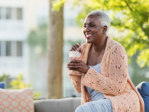 A Black Woman Enjoys a Smoothie on a Bench Outside