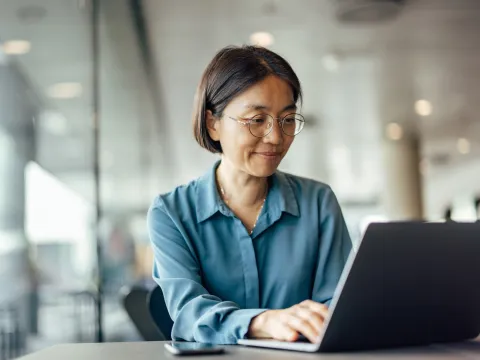 A woman sitting at a table using a laptop while indoors.