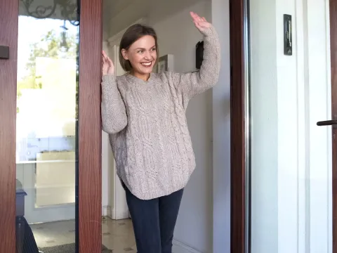 A woman waving at her neighbors from her porch.